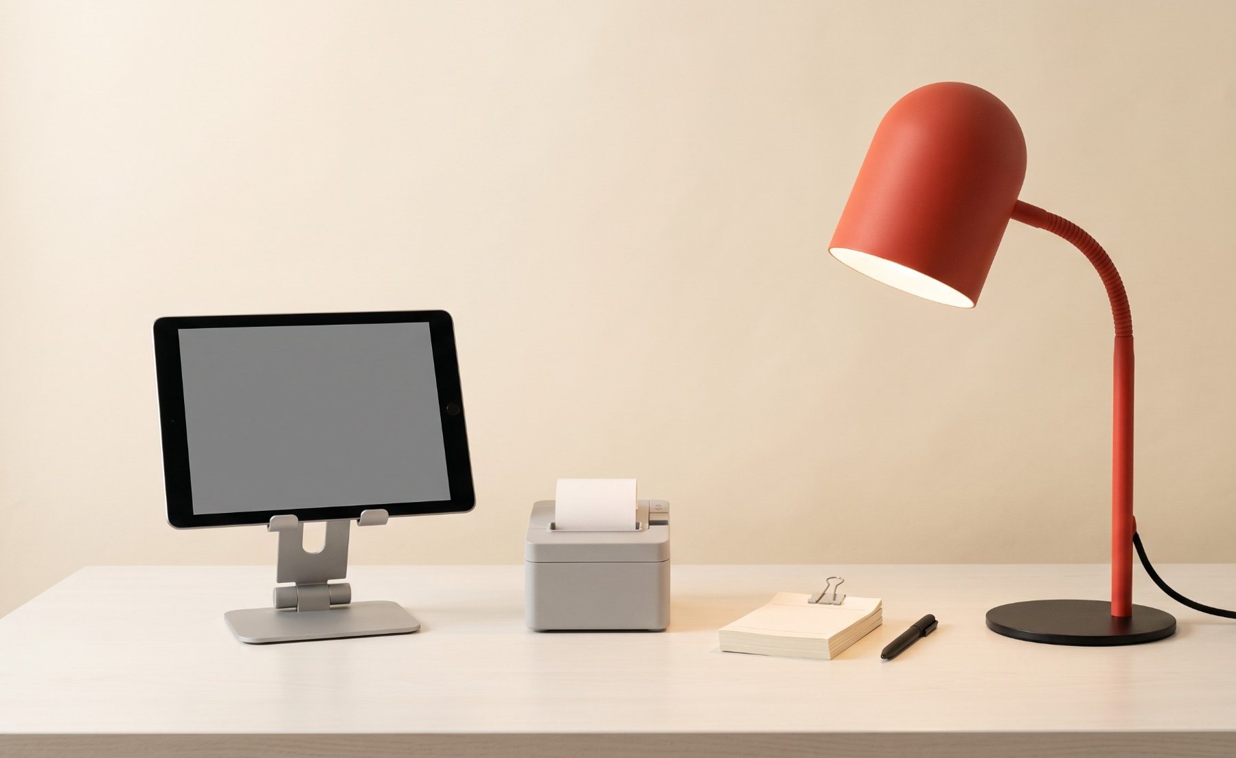 A tidy counter with a tablet on a stand, a receipt printer and a red desk lamp